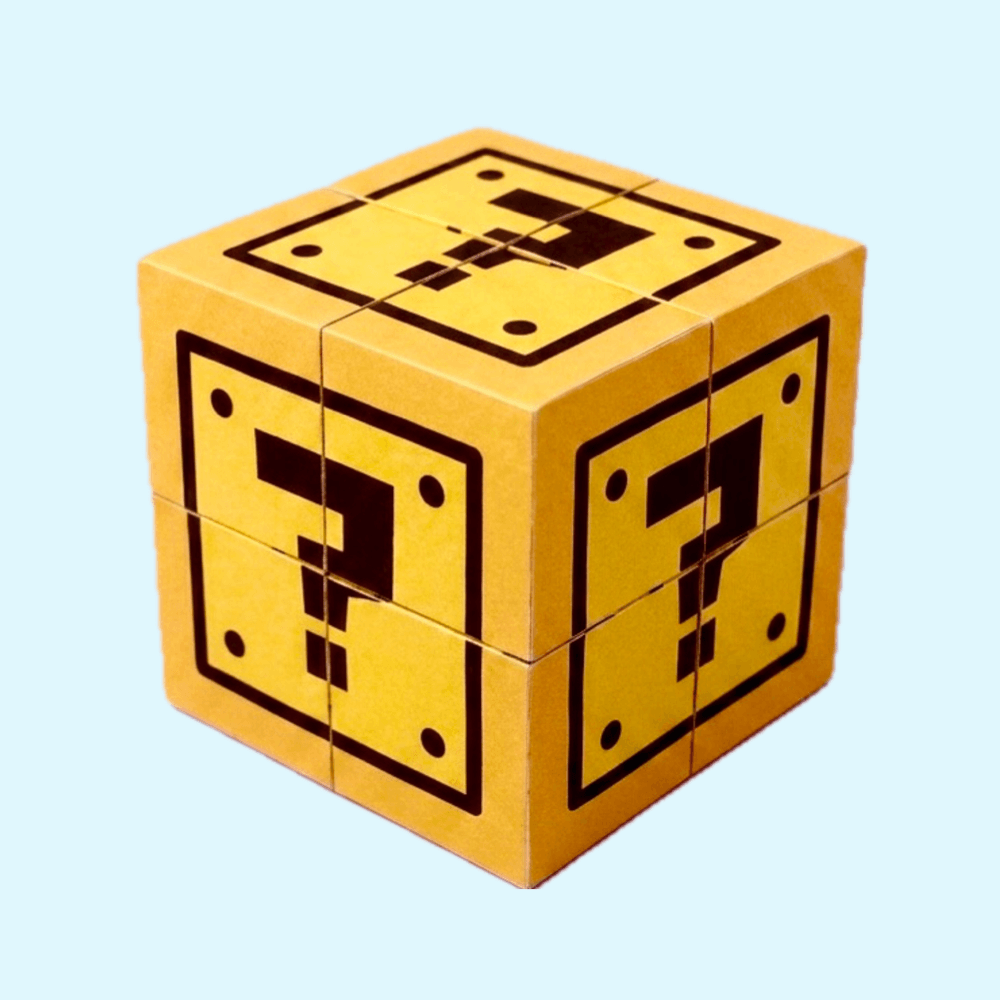 A 3D DIY paper craft cube designed to look like a Super Mario yellow question block, made of interlocking square panels, shown on a light blue background.